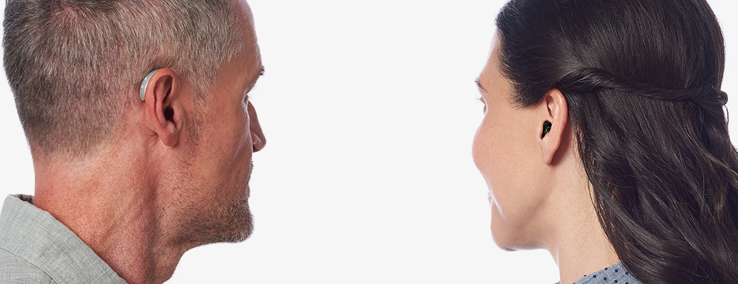 Image of man wearing standard hearing aid and woman wearing custom hearing aid